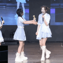 a girl in a blue dress is holding a microphone while another girl stands behind her