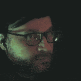a man with glasses and a beard looks at the camera in the dark