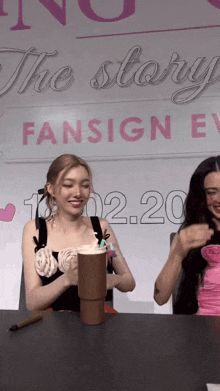 two women are sitting at a table in front of a sign that says the story fansign ev