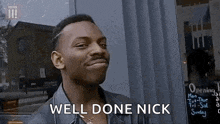 a man is smiling and saying `` well done nick '' in front of a store window .