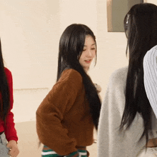 a woman with long black hair wearing a brown sweater stands next to another woman