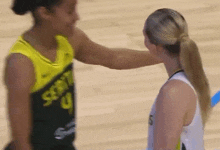 two female basketball players are touching each other 's faces on the court .
