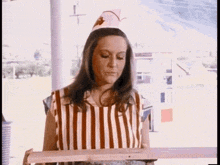 a woman wearing a striped apron and a hat is holding a wooden plank .