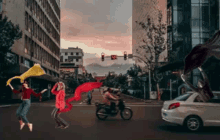 a man on a motorcycle is driving down a city street with people dancing in the background