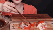 a woman is eating sushi with chopsticks on a wooden board .