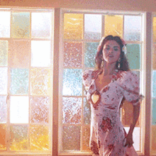 a woman in a floral dress is standing in front of a window with stained glass
