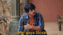 a man in a plaid shirt is sitting down with the words mar gaya shiva written above him