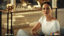 a woman in a white dress sits on a couch with a nbc logo on the bottom