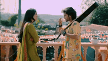 a man and a woman are standing on a balcony and the man is drinking from a cup while the woman looks on