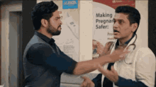 two men are talking in front of a sign that says " making pregnant safer "