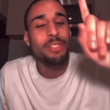 a man with a beard wearing a white t-shirt is giving the middle finger