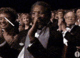 a man in a tuxedo is applauding in front of a crowd