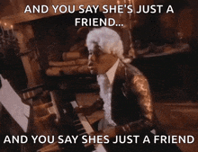 a man in a wig is playing a piano with the caption " and you say she 's just a friend ... "