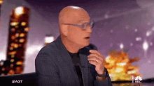 a bald man wearing glasses and a plaid jacket is sitting in front of a nbc sign