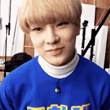 a young man with blonde hair is wearing a blue sweater and a white turtleneck sweater .