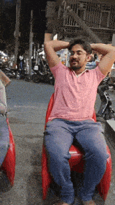 a man in a pink shirt is sitting on a red chair with his hands behind his head