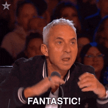 a man with a microphone says fantastic in front of a crowd of people