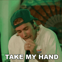 a man in a green hat is singing into a microphone and the words take my hand are above him