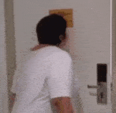 a woman in a white shirt is standing in front of a door with a yellow sign on the wall behind her .