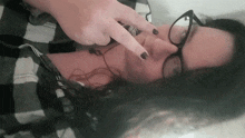 a woman wearing glasses and a plaid shirt is pointing her finger at her face