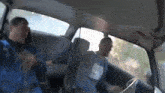 a man in a blue nike shirt is driving a car with another man in the back seat .