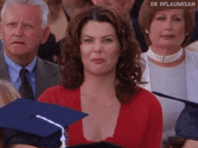 a woman in a red top is sitting in a crowd of people with a graduation cap on .