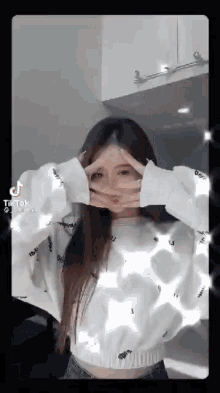 a woman in a white sweater is making a funny face with her hands in front of her face .