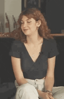 a woman with curly hair is sitting on the floor with her eyes closed and smiling .