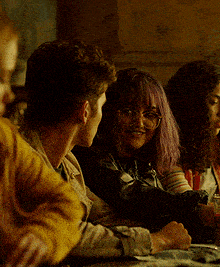 a group of people are sitting at a table and one of them has glasses on