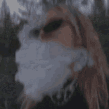a woman wearing sunglasses is smoking a cigarette in front of trees .