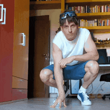 a man squatting down in front of a bookshelf with a bottle of coca cola
