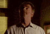 a man with a beard and a white shirt is looking up at something in the dark .