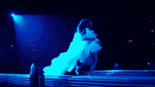a woman in a white dress is dancing on a stage with a blue light behind her