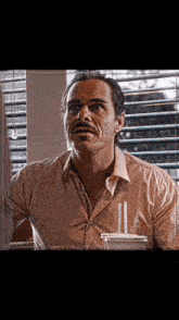 a man with a mustache is sitting in front of a window with blinds ..