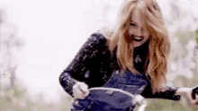 a woman wearing overalls is laughing while holding a book .