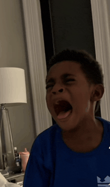 a young boy in a blue shirt is screaming with his mouth open