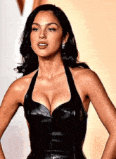 a woman in a black leather dress with a plunging neckline is standing with her hands on her hips .