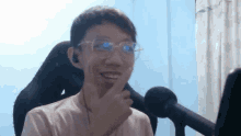 a man wearing glasses and ear buds is sitting in front of a microphone and smiling .
