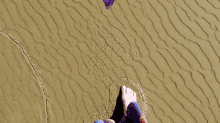 a person 's feet are standing on a sandy surface
