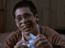 a man wearing glasses and a brown jacket is laughing