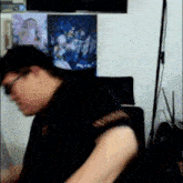 a man in a black shirt is sitting in front of a wall with posters on it