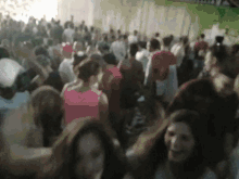 a blurred image of a crowd of people including a woman in a pink shirt