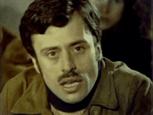 a man with a mustache is wearing a brown jacket and a black scarf around his neck