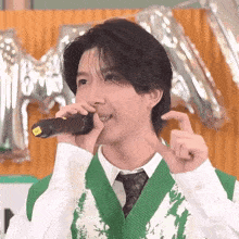 a young man is singing into a microphone while wearing a green vest and tie .
