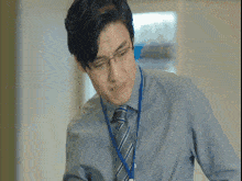 a man in a blue shirt and tie is wearing glasses and a lanyard around his neck .