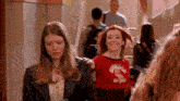 two girls are walking down a hallway and one of them is wearing a red shirt that says ' chicago ' on it .