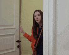 a woman in an orange jacket is peeking out of a door