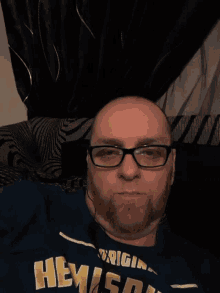 a man wearing glasses and a shirt that says hemingway is laying on a bed