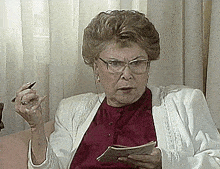 an elderly woman wearing glasses and a white jacket holds a pen