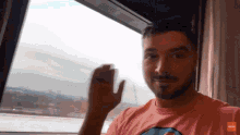 a man in a pink shirt is waving his hand in front of the window
